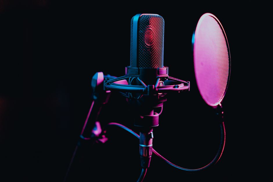 Side-address condenser microphone in a shock mount with a pop filter, lit in a dark studio